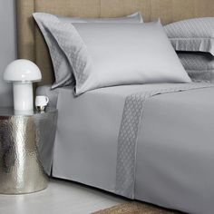 a bed with silver sheets and pillows on top of it next to a night stand