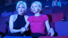 two women sitting in the middle of a movie theater, one with her hand on another's shoulder