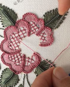 someone is stitching flowers on a piece of white fabric with pink and green thread