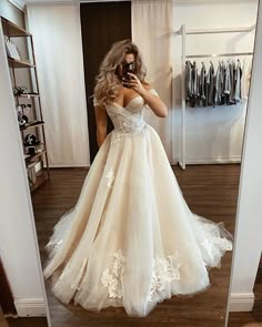 a woman in a wedding dress taking a selfie with her cell phone while standing in front of a mirror