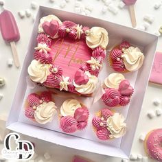 pink and white cupcakes are arranged in a heart shaped box on a table