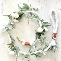 a wreath made out of white flowers and greenery on a wooden background with rope