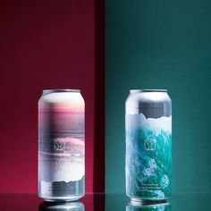 two cans of soda sitting next to each other on top of a glass table in front of a red and green wall