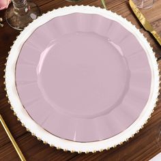 a pink plate sitting on top of a wooden table next to utensils and wine glasses