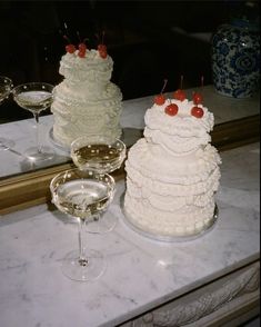 there are two cakes on the counter with wine glasses next to it and one cake has cherries on top