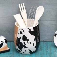 two black and white utensils are in a cow print cup with spoons