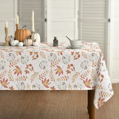 a table topped with a white and orange fall themed table cloth next to two pumpkins