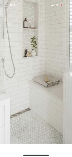 a white tiled bathroom with a shower, sink and shelf above the bathtub is an open shelving unit