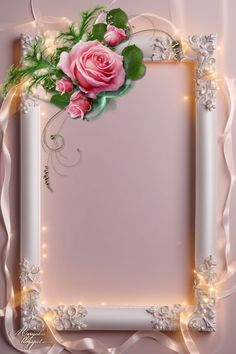 a white frame with pink roses and green leaves on the edge is surrounded by lights