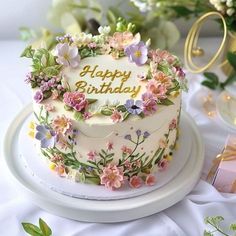 a birthday cake decorated with flowers and the words happy birthday written on it in gold lettering