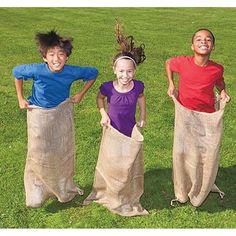 three children are standing in the grass with their hands on their hipss and one is holding a sack