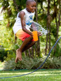 a young boy jumping in the air with a water hose