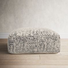 a white and black ottoman sitting on top of a hard wood floor next to a wall