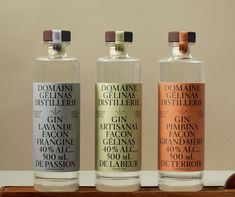 three bottles of different types of gin in front of a white wall and wooden tray