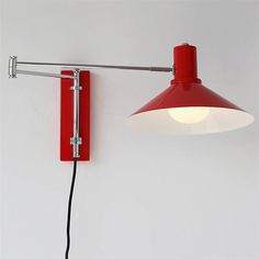 a red wall mounted lamp with a white light on it's side and a black cord attached to the arm