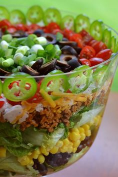 a salad in a glass bowl with tomatoes, black olives, lettuce and other vegetables