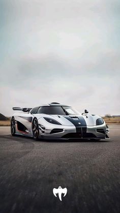 a white and black sports car driving down a road with clouds in the sky behind it