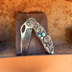 a knife sitting on top of a piece of metal next to a stone block with turquoise stones