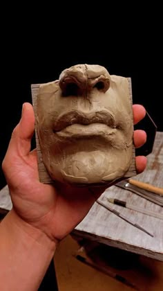 a person holding up a clay face on a piece of wood