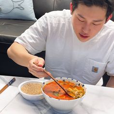 a man sitting at a table with a bowl of soup and chopsticks