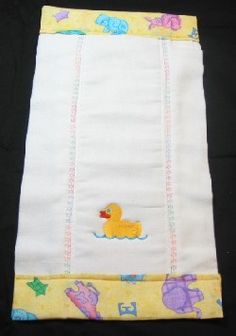 a white towel with yellow rubber ducky embroidered on the front and bottom, sitting on a black surface