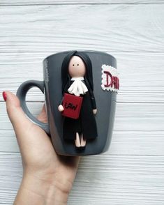 a hand holding a coffee mug with a doll in it