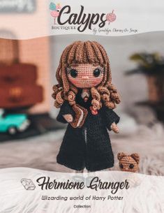 the doll is wearing a black coat and holding a teddy bear in her hands, sitting on a bed