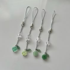 four pairs of dangling earrings with green and white flowers on them, hanging from silver chains