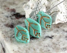 three pairs of turquoise and gold leaf earrings on a marble countertop next to a rock