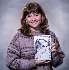 a woman is holding up a book in front of her face and smiling at the camera