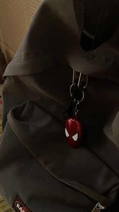 a black backpack with a spiderman face on the front pocket and a red keychain hanging from it