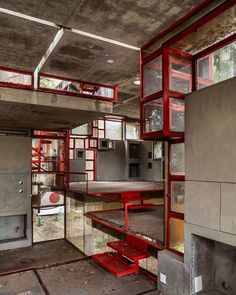 an abandoned kitchen with red shelves and stairs leading up to the upper floor, surrounded by concrete walls