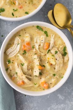 two bowls of chicken and dumpling soup with spoons next to it on a gray surface