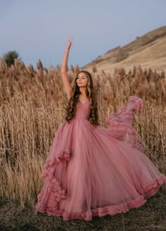 a girl in a pink dress standing in a field with her arms up and smiling at the camera