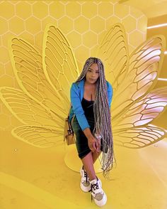 a woman sitting on top of a yellow bench next to a giant butterfly shaped object