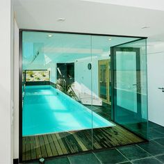 an indoor swimming pool with glass walls and wooden flooring is seen from the outside