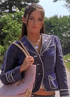 a woman carrying a pink handbag while walking down a street with trees in the background