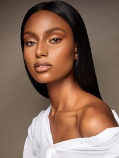 a woman with long black hair wearing a white shirt and gold eyeshadow on her face