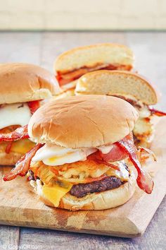 three burgers with bacon, cheese and eggs on a cutting board