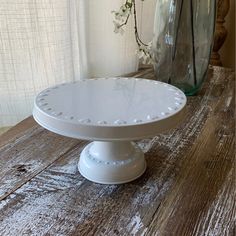 a white cake plate sitting on top of a wooden table next to a vase filled with flowers