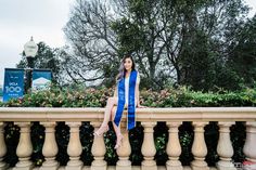 a young woman sitting on top of a stone bench wearing a blue graduation sash and posing for the camera