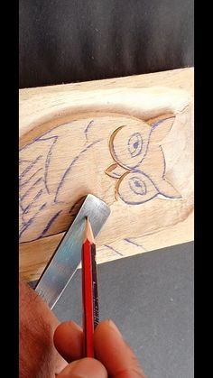 a person holding a pencil and sharpener in front of a carved wooden object with an owl on it