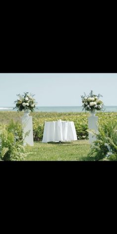 an outdoor ceremony setup with white linens and greenery on the grass near the ocean