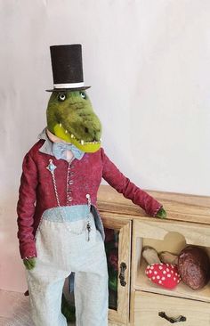 a stuffed alligator in a top hat and sweater standing next to a dresser with drawers