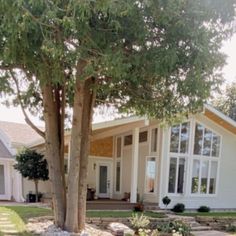 a large white house sitting next to a lush green tree in the middle of a yard