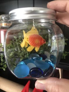 a goldfish in a glass jar filled with blue and yellow sea glass stones,