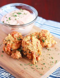 some food is sitting on a cutting board next to a bowl of dip and sauce