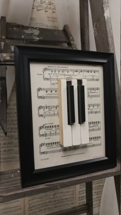 a framed musical score with piano keys and sheet music in black frame on wooden shelf