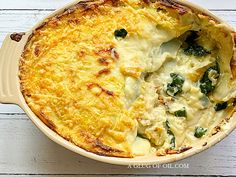 a casserole dish with cheese and spinach in it on a white wooden table