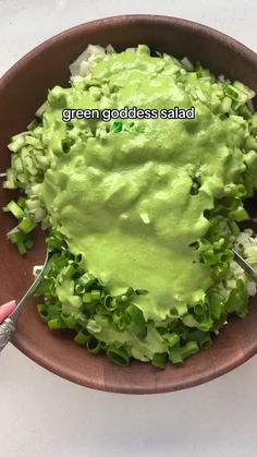 a bowl filled with lettuce and topped with green goddess salad dressing next to a hand holding a fork